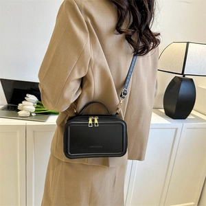 Minimalist black suitcase-style crossbody bag with gold zippers and adjustable strap