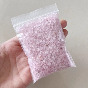 Close-up of hand holding a transparent bag filled with natural pink quartz crystal stones