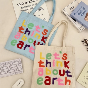 Flat lay of canvas tote bags with colorful towel embroidery and eco-friendly earth slogans