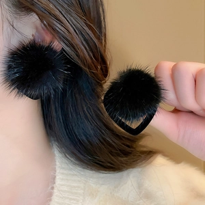 Close-up of fluffy black heart-shaped plush earrings worn by a model in soft light