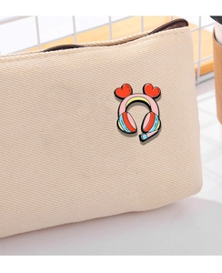 Close-up of a pink cartoon headphone enamel pin with heart accents on a beige canvas bag