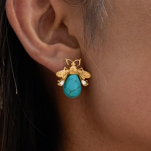 Close-up of a gold bee stud earring with turquoise stone worn on the earlobe