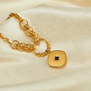Macro shot of gold square pendant and striped beads on a smooth beige velvet texture