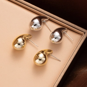 Close-up of gold and silver teardrop stud earrings with a polished mirror finish