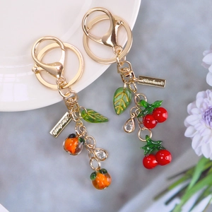 Detailed close-up of handmade cherry and orange fruit keychains with sparkling crystals