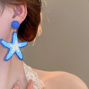 Close-up of a blue and white raffia woven starfish earring worn by a female model