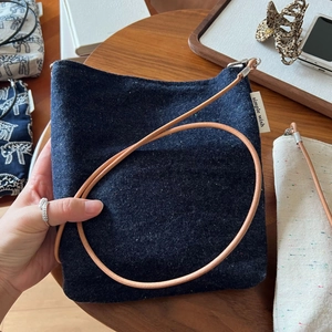 Detail of blue denim crossbody bag with embroidered label and slim brown leather strap