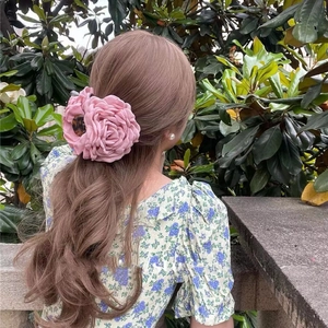 Pink fabric camellia flower hair claw clip worn by a model in an outdoor setting
