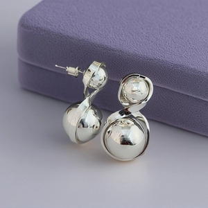 Minimalist silver dual ball stud earrings with twisted metal design on a purple display