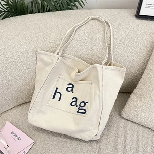 Close-up of the front pocket on a beige canvas tote bag with navy letter printing