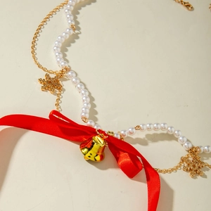 Detail of Christmas necklace with white pearls, red ribbon bow, and golden snowflake charms