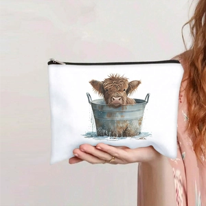 Close-up of highland cow print cosmetic bag held in hand, showing canvas texture and zipper