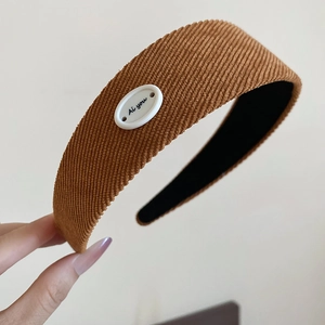 Détail d'un serre-tête en velours côtelé marron avec écusson blanc et lettrage Ai you