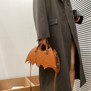 Detail of orange bat-shaped handbag with spider web stitching and crossbody strap