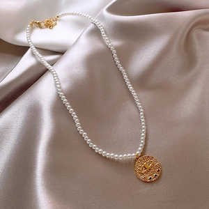 Macro view of gold plated pearl necklace featuring an evil eye coin pendant on silk