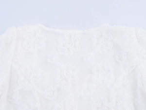 Detailed macro view of white 3D rose floral embroidery on lace mesh neckline
