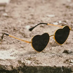 Fashion heart shaped sunglasses with gold metal frame and black lenses on stone surface