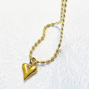 Luxurious gold heart pendant necklace with fine ball chain on a textured white surface