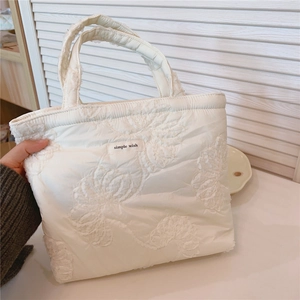 Close-up of cream quilted tote bag featuring floral lace embroidery and a 'simple wish' tag