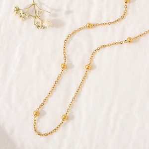 Detail of elegant gold beaded cable chain necklace on a soft textured cream fabric