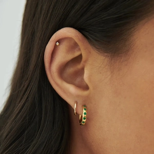 Close-up of a model wearing a gold earring set with green stones and a sparkling stud