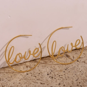 Detail of 18K gold plated hoop earrings with artistic Love script on a stone surface