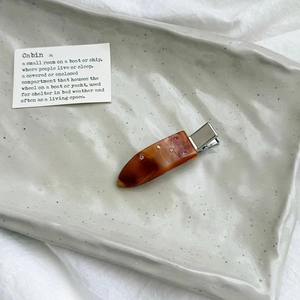 Close-up of marble pattern resin hair clip with colorful rhinestones on a ceramic plate