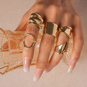 Close-up of five-piece gold geometric ring set worn on hand holding a glass