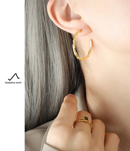 Detailed view of gold-plated stainless steel C-shaped hoop earrings and green gemstone ring