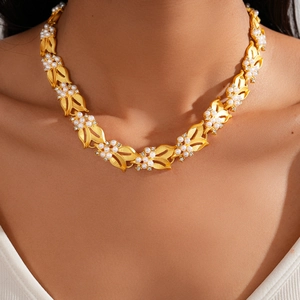 Dettaglio collana vintage dorata con ciondoli a foglia, perle bianche e zirconi