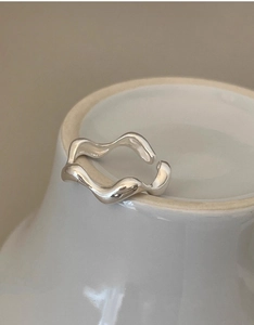 Macro shot of silver wavy irregular stackable ring on a white ceramic display