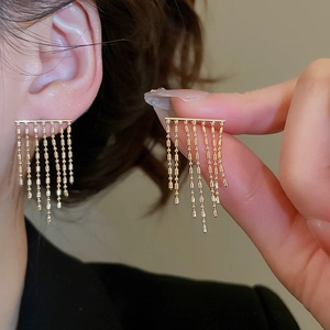 Close-up of golden fringe tassel earrings with vertical bar and bead chain details