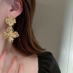 Close-up of golden metallic flower drop earrings worn by a model in soft lighting