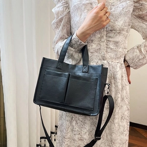 Detail of black pebbled tote bag with front pockets and adjustable shoulder strap