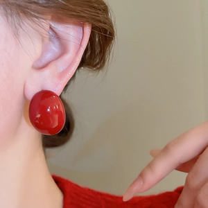 Close-up of a large red spherical stud earring with high-gloss finish worn by a model
