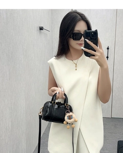 Mirror selfie of a black glossy Boston bag with plush pendant and adjustable strap