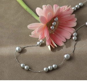 Detailed view of long grey pearl necklace with silver chain over floral background