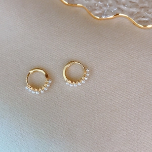 Elegant gold hoop earrings with small pearls on beige fabric background, chic style