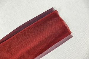 Macro detail of wine red sheer mesh fabric with layered texture on a ruched evening dress