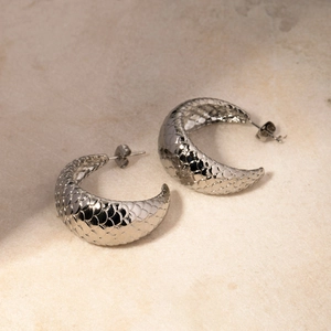 Detailed shot of silver C-shape earrings with unique scale texture on matte stone background