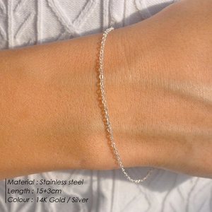 Minimalist gold stainless steel thin chain bracelet for women on textured white fabric