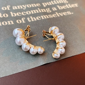Macro shot of curved gold pearl earrings with five white pearls on a dark background