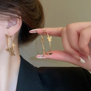 Detail showing large gold hoop earrings with butterfly motifs worn with a black blazer