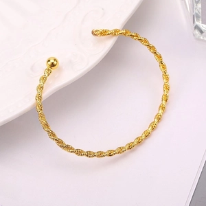 Elegant gold twisted cable open cuff bracelet with polished bead ends on a white ceramic plate