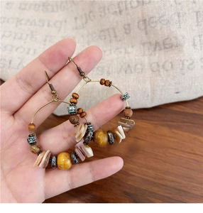 Detail of bohemian hoop earring with wooden beads and shell fragments in hand