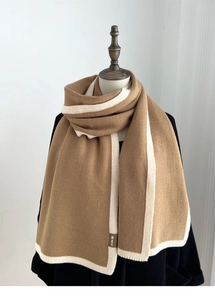 Detail of knitted scarf with camel and white contrast edging and leather logo patch