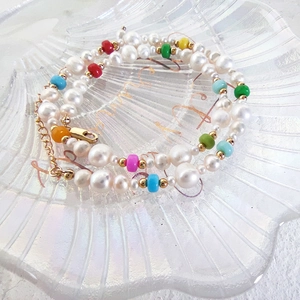 Detail of baroque pearl choker with colorful beads and gold lobster clasp on glass tray