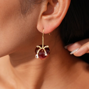 Gros plan de boucles d'oreilles cerises en résine rouge et feuilles de zircon sur oreille