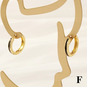 Detail of 18K gold hoop earrings with black enamel inlay on an artistic jewelry stand