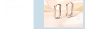 Macro detail of silver U-shaped stainless steel hoop earrings on soft silk fabric